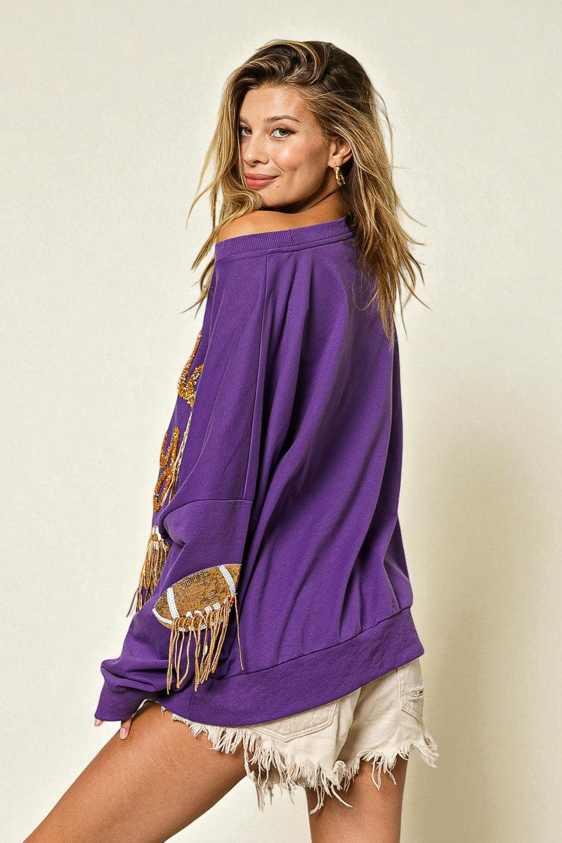 Woman wearing a purple off-shoulder top with fringe details on a plain background