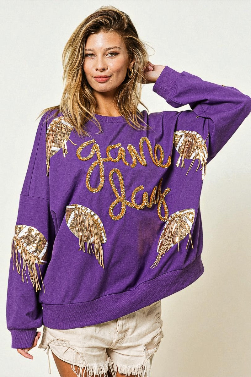 Woman wearing a purple sweatshirt with gold 'game day' text and angel wing designs on a plain background