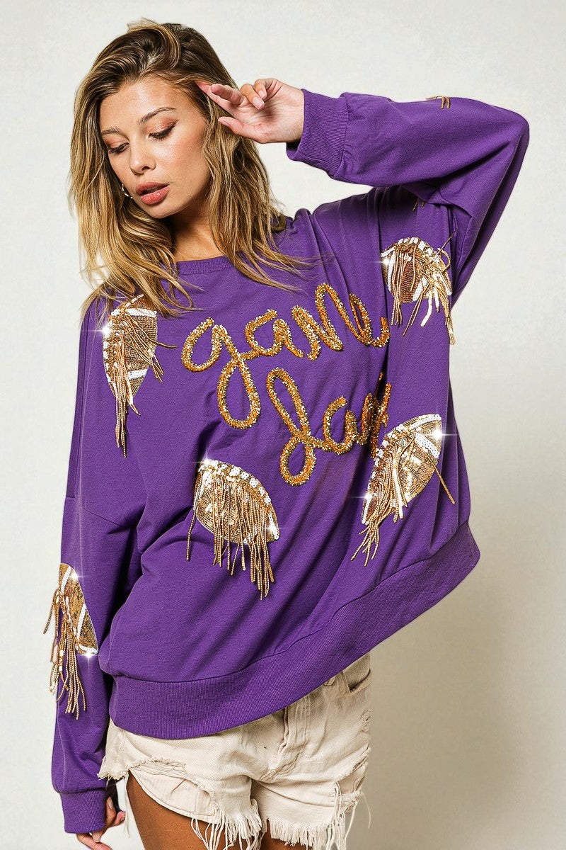 Woman wearing a purple sweatshirt with gold designs and text on a plain background