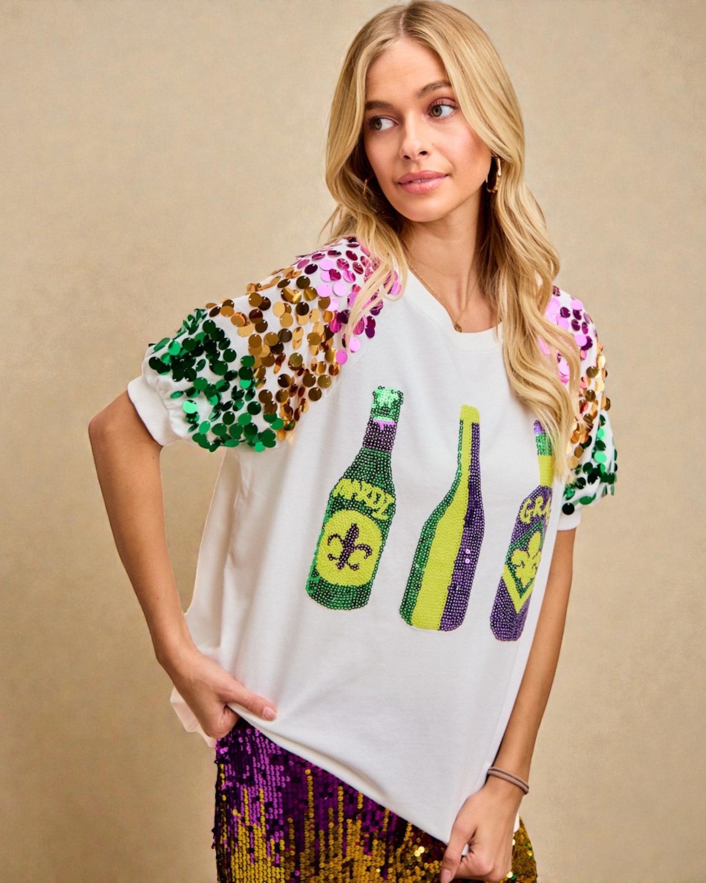 Woman wearing a white t-shirt with colorful sequin sleeves and bottle graphic on a beige background