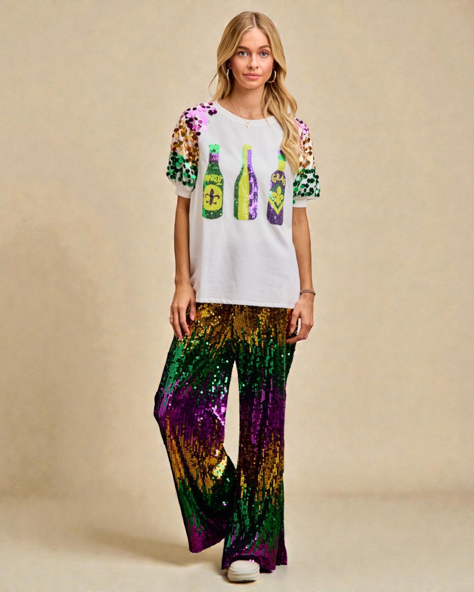 Woman wearing a colorful top with bottle graphics and sequin pants on a beige background