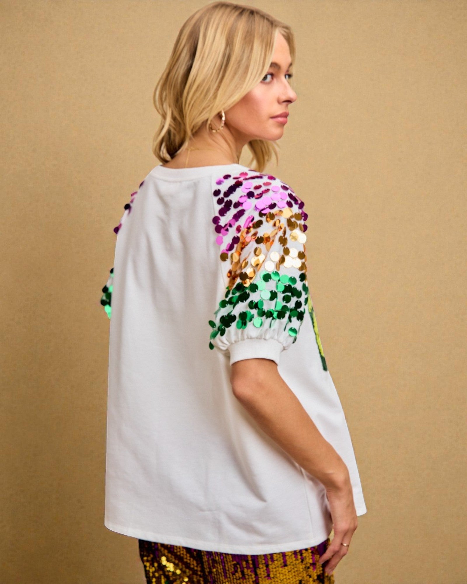 Woman wearing a white top with colorful sequin sleeves against a beige background