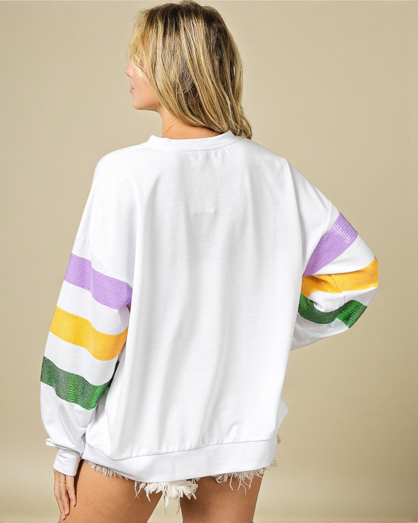 Person wearing a white sweatshirt with colorful sleeves on a beige background