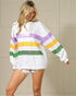 Woman wearing a white sweater with colorful stripes against a beige wall.