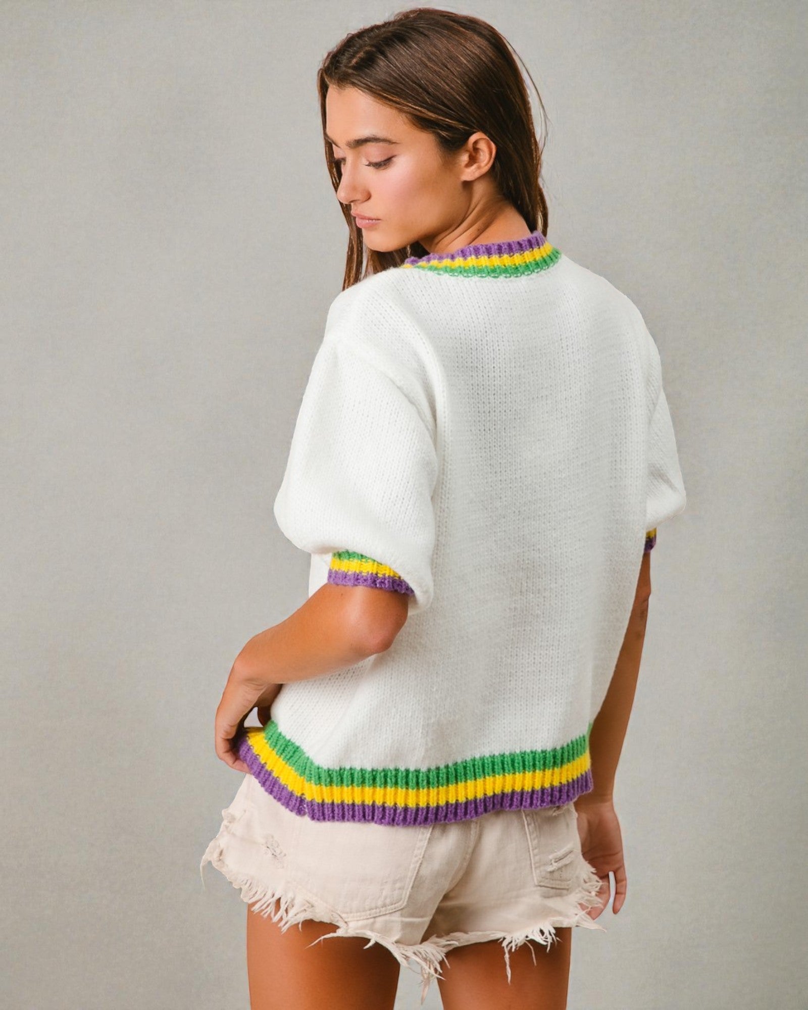 Woman wearing a white sweater with colorful trim on a gray background