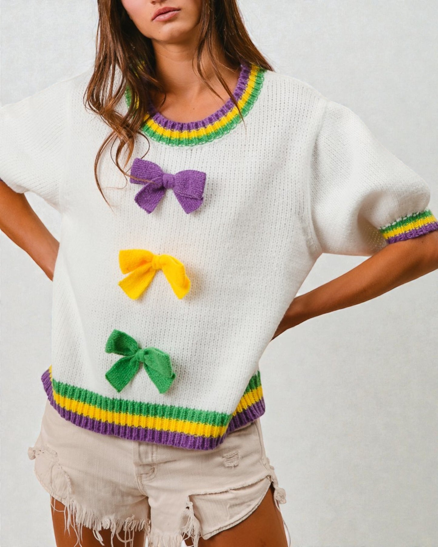 White sweater with colorful trim and bows worn by a person on a white background