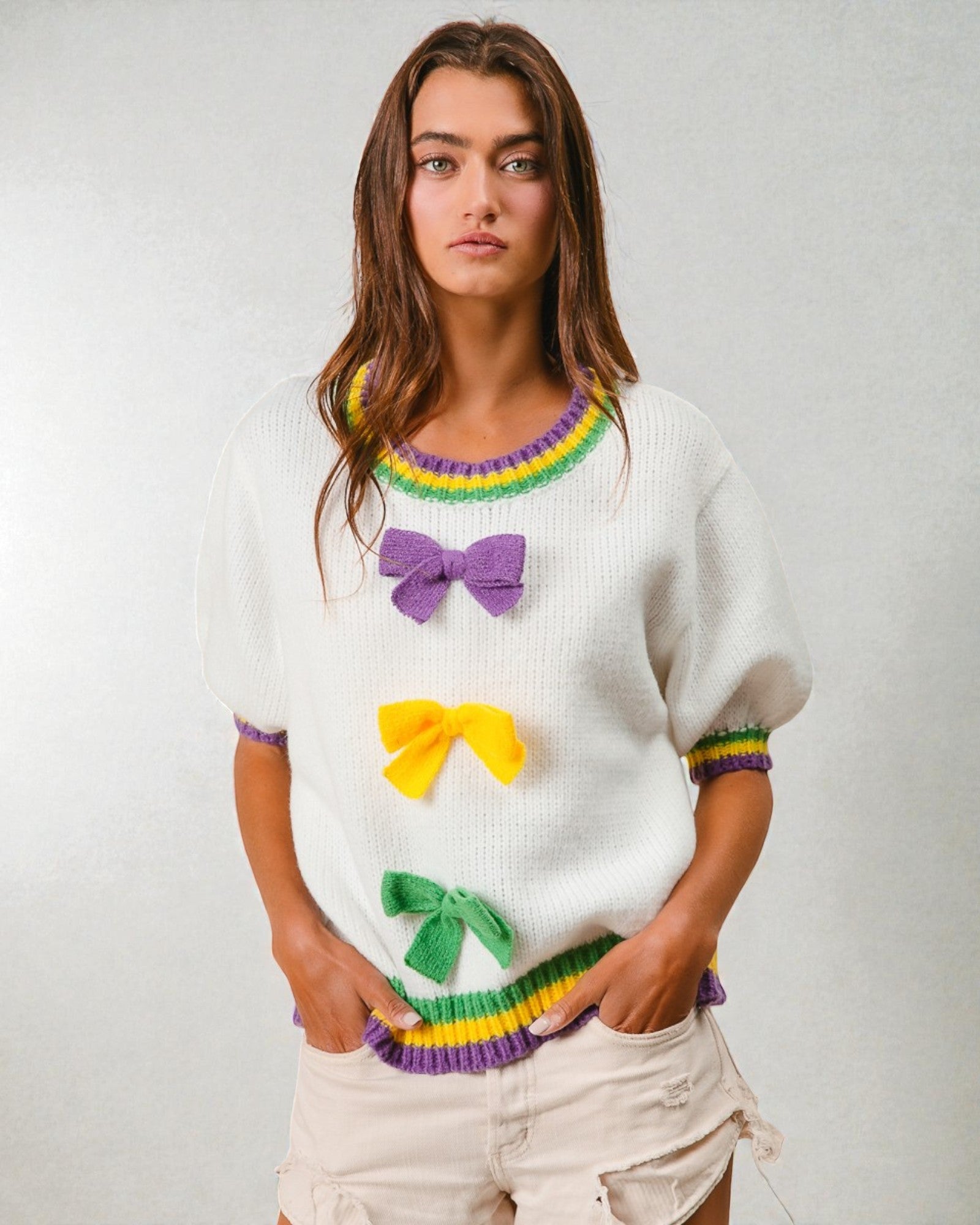 Model wearing a colorful sweater with bows on a plain background