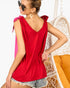A woman wearing a bright red sleeveless top with tie-shoulder details and a V-neckline, paired with denim shorts, shown from the back in a lifestyle setting next to a hanging chair.