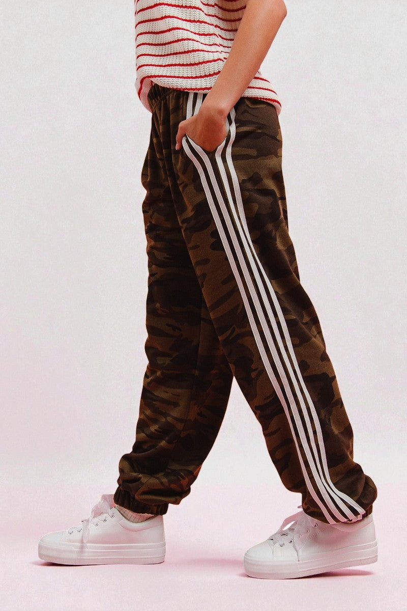 Camouflage pants with white stripes worn by a person on a pink background