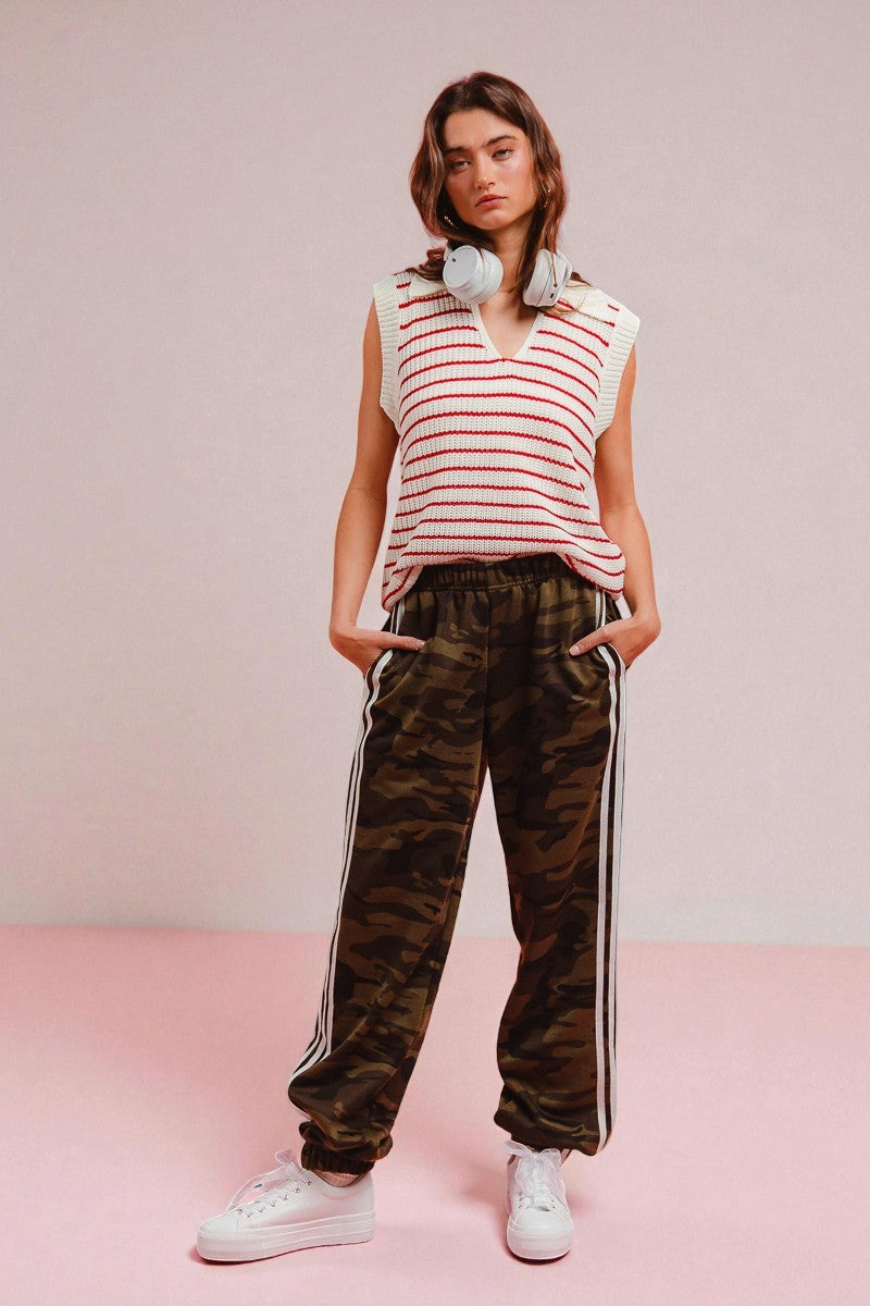 Woman wearing a striped sleeveless top and camouflage pants with white stripes on a pink background
