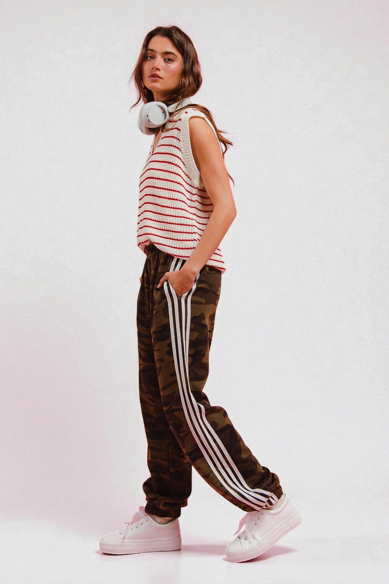 Woman wearing a striped top and camouflage pants with white stripes on a white background