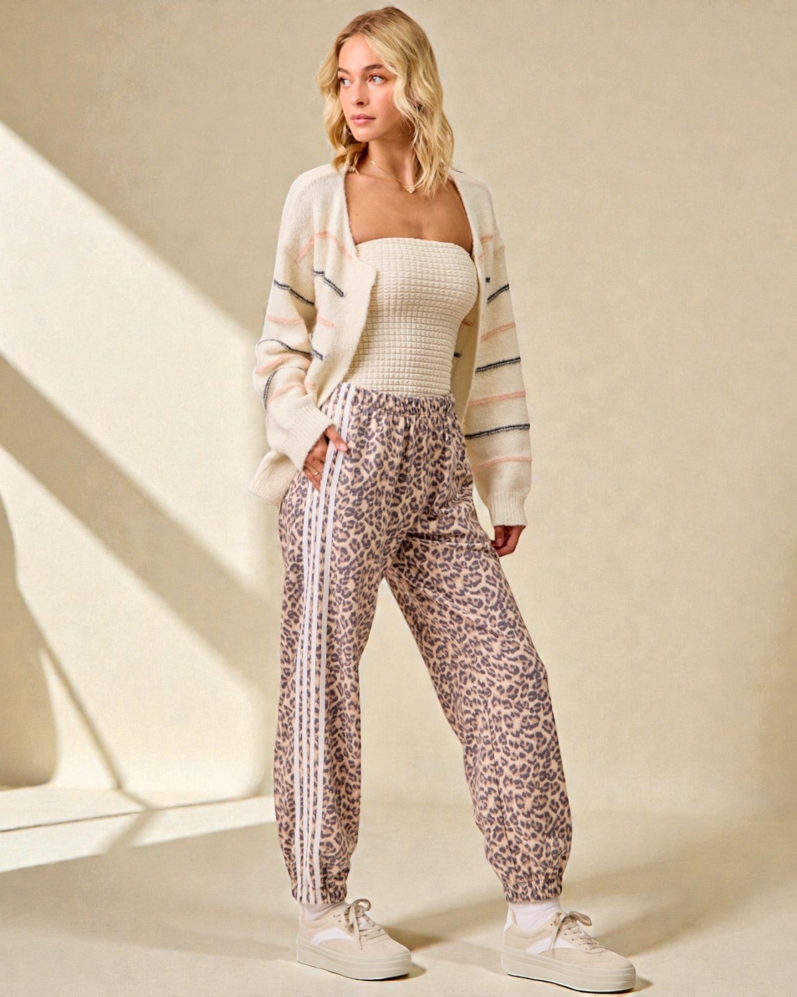 Woman wearing a white cardigan, white top, and leopard print pants on a beige background