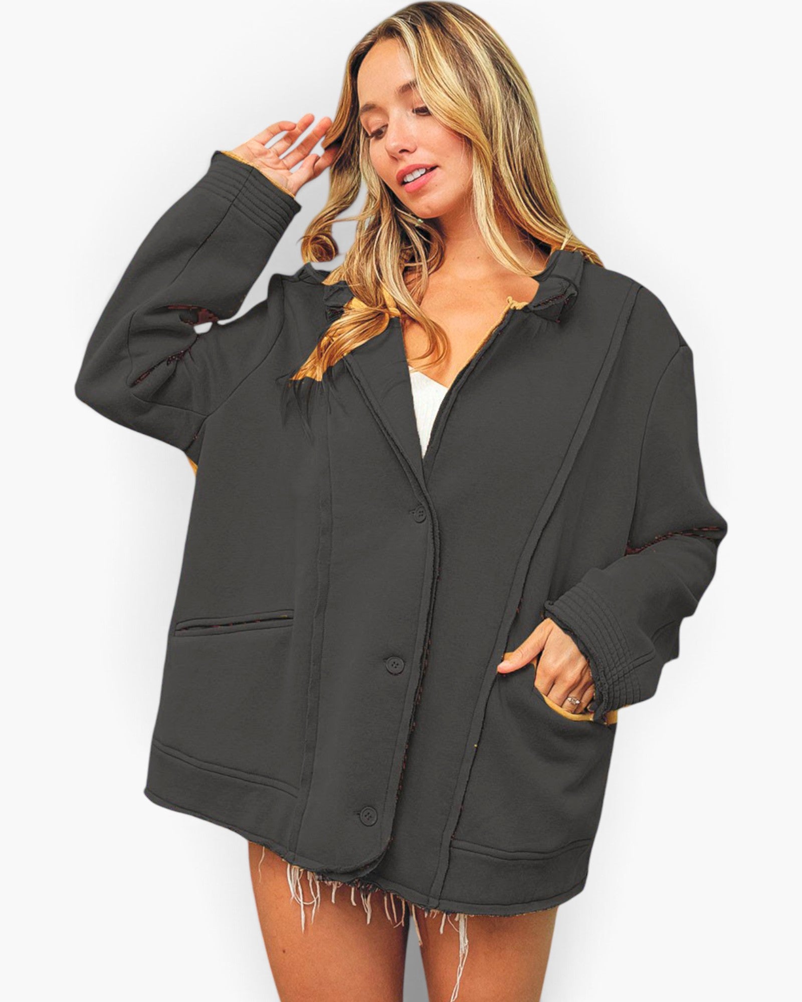 A woman modeling an oversized dark charcoal gray jacket with a button front, ribbed cuffs and hem, and contrast tan lining in the pockets, set against a plain white background.
