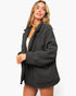 A woman modeling an oversized black jacket with a soft, slightly textured fabric, shown against a plain white studio background.