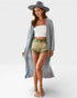 Woman wearing a long gray cardigan, white top, and green shorts on a white background