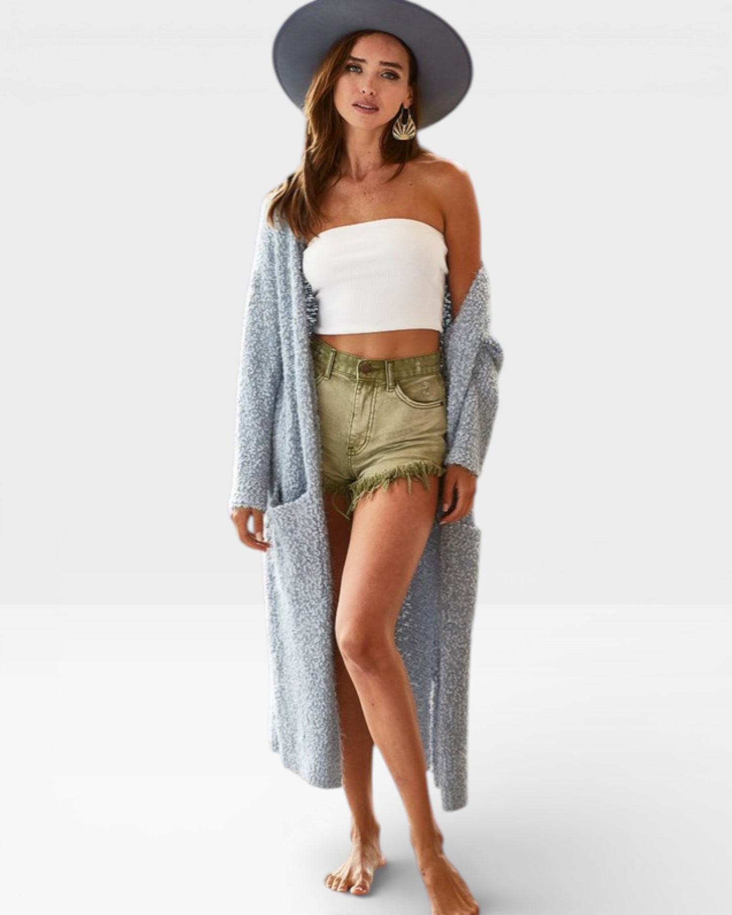 Woman wearing a long gray cardigan, white top, and green shorts on a plain background