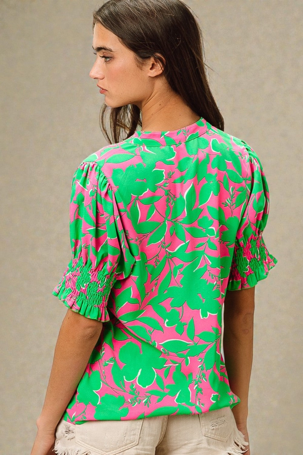 Woman wearing a green and pink floral blouse against a neutral background