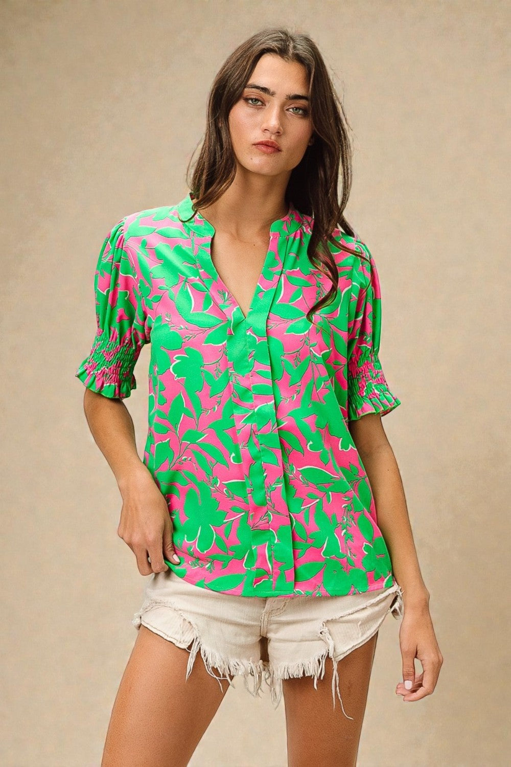 Woman wearing a green and pink patterned blouse with white shorts on a beige background