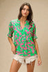 Woman wearing a green and pink patterned blouse with white shorts on a beige background