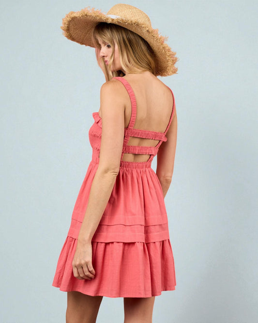 Woman wearing a pink dress with cut-out design and a straw hat on a light gray background