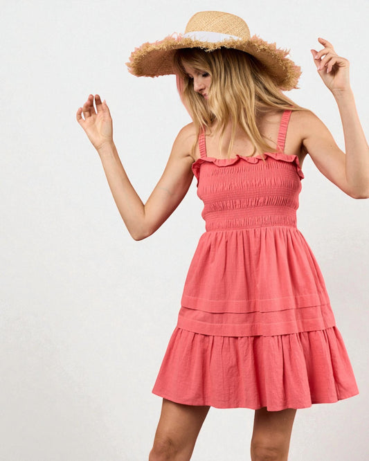 Woman wearing a coral dress and wide-brimmed hat on a plain background