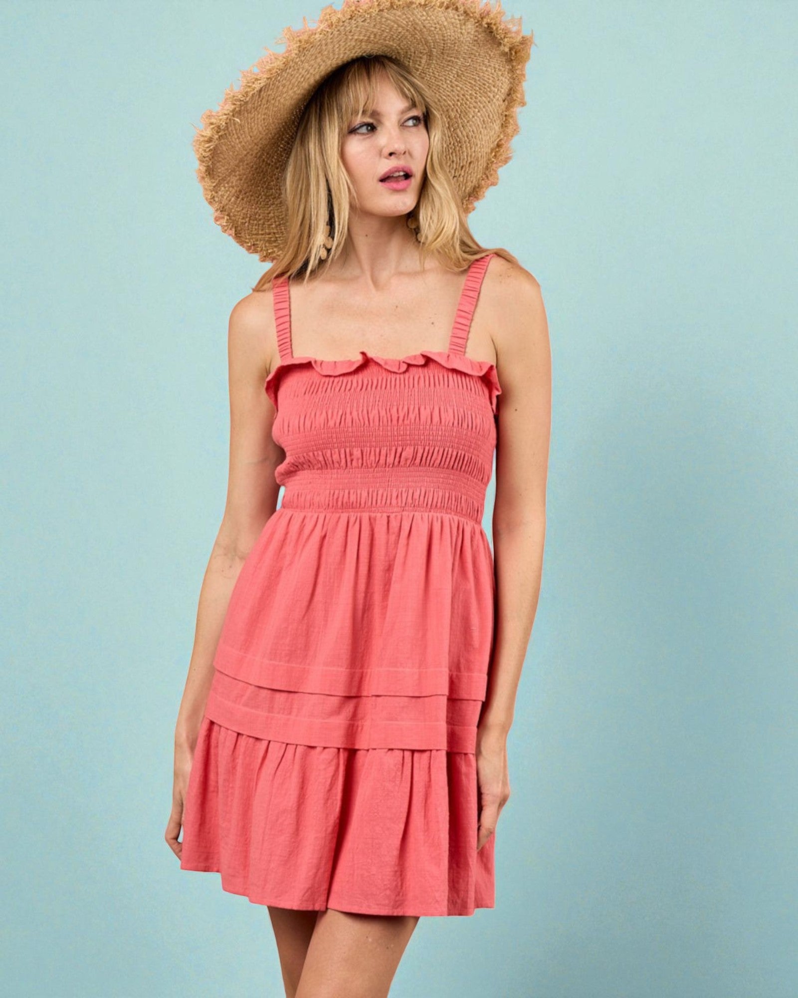 Woman wearing a coral dress and straw hat against a light blue background