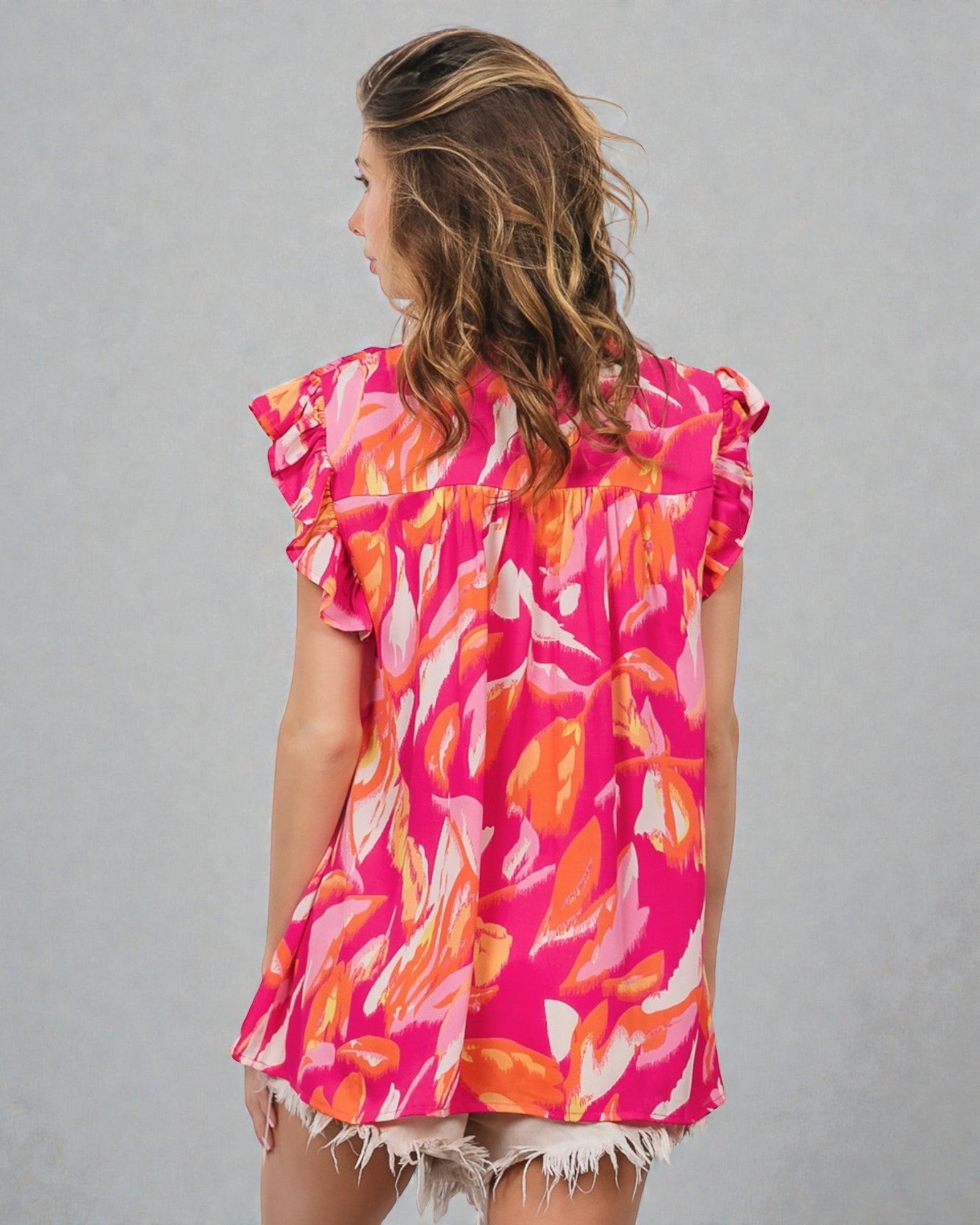 Woman wearing a colorful pink and orange patterned top against a gray background