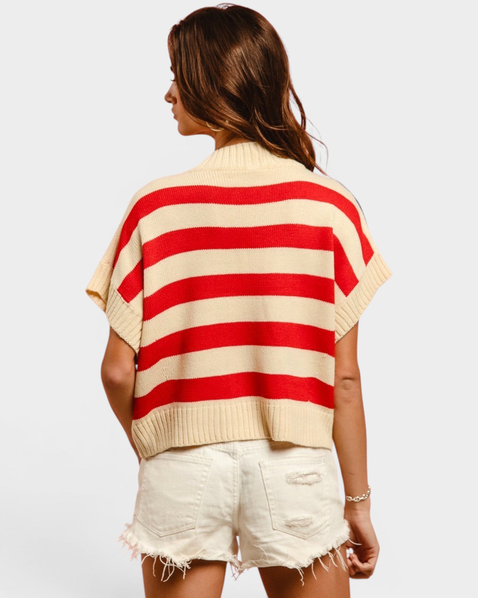 Woman wearing a red and beige striped sweater with white shorts on a plain background