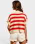 Woman wearing a red and beige striped sweater with white shorts on a plain background