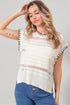 Woman wearing a white crochet top with black trim against a gray background