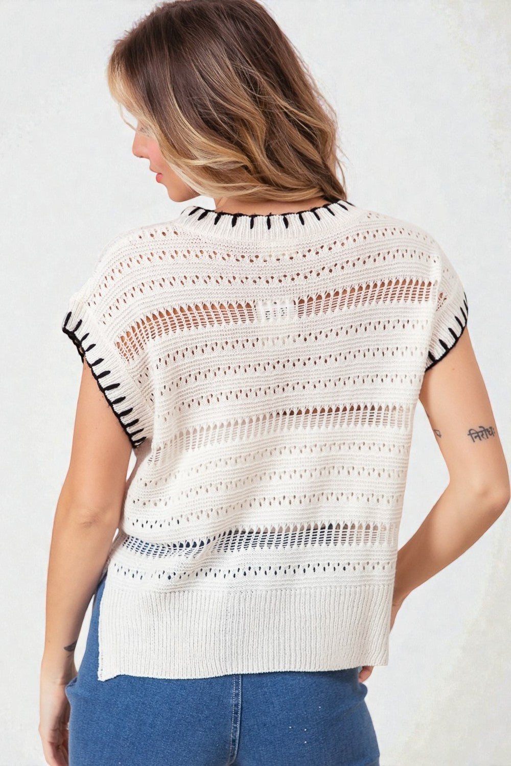 Woman wearing a white knit top with black patterned sleeves on a plain background