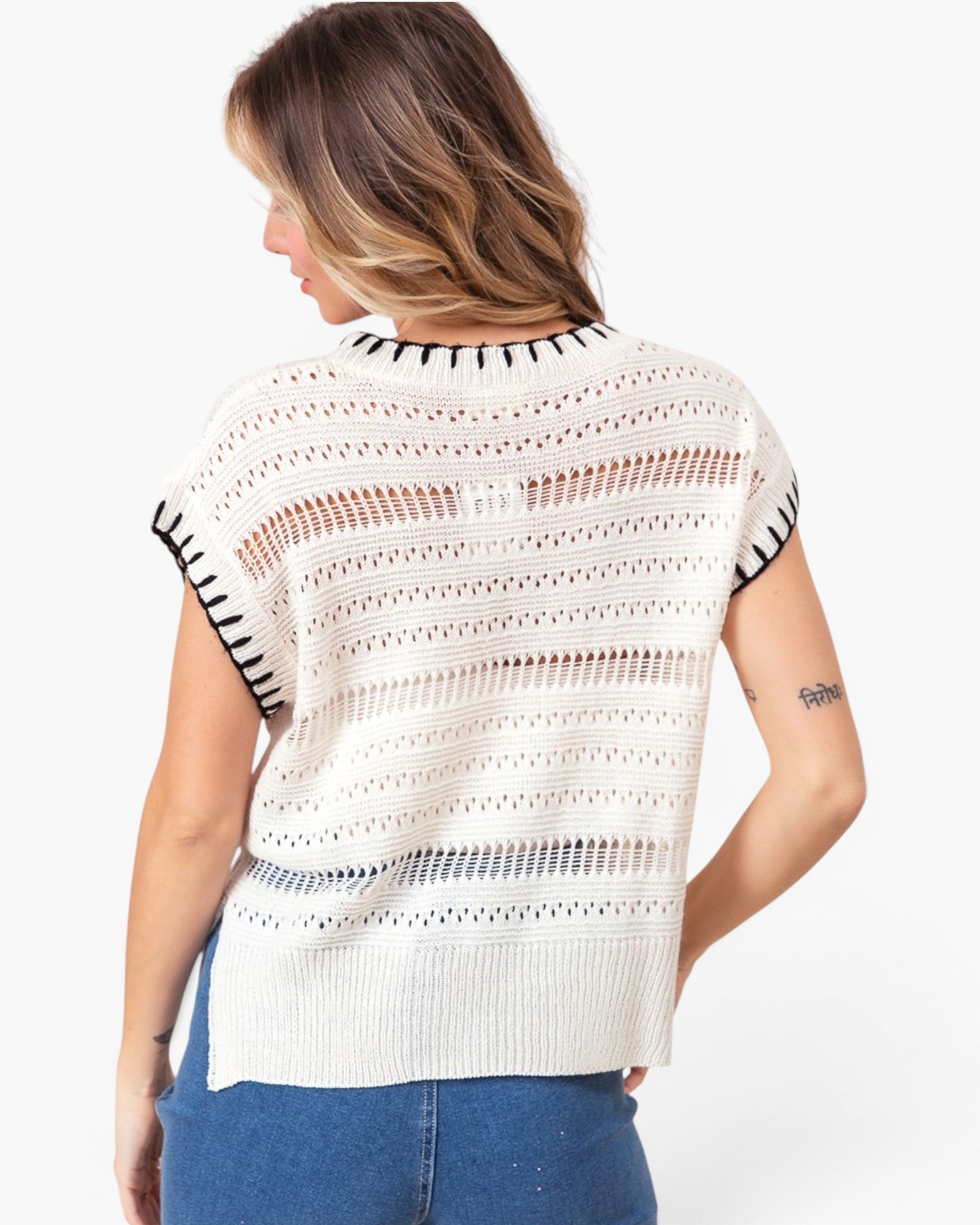 A woman shown from the back wearing a cream-colored open-knit short-sleeve top with black striped sleeve cuffs, paired with blue jeans, against a plain white background.