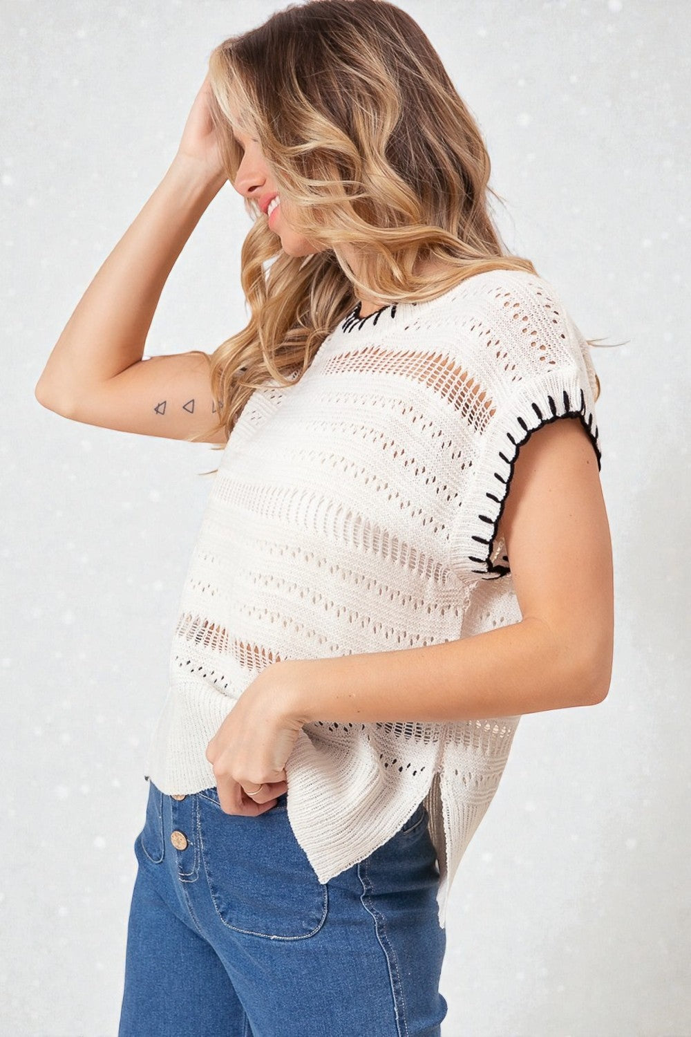Woman wearing a white crochet top with black accents and blue jeans on a white background