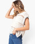 A woman wearing a cream-colored, short-sleeve knit top with black contrast stitching along the sleeve edges, paired with blue jeans, photographed against a plain white background.