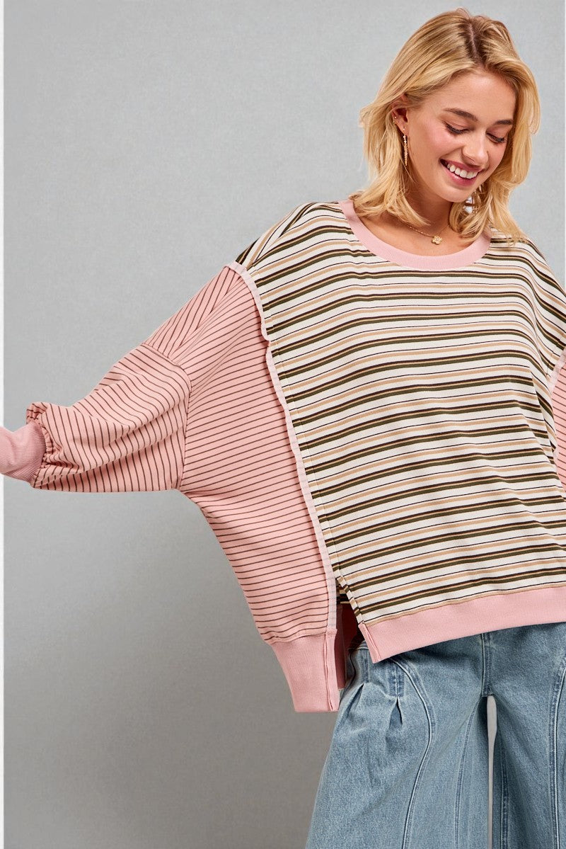 Woman wearing a striped sweater with pink sleeves against a gray background