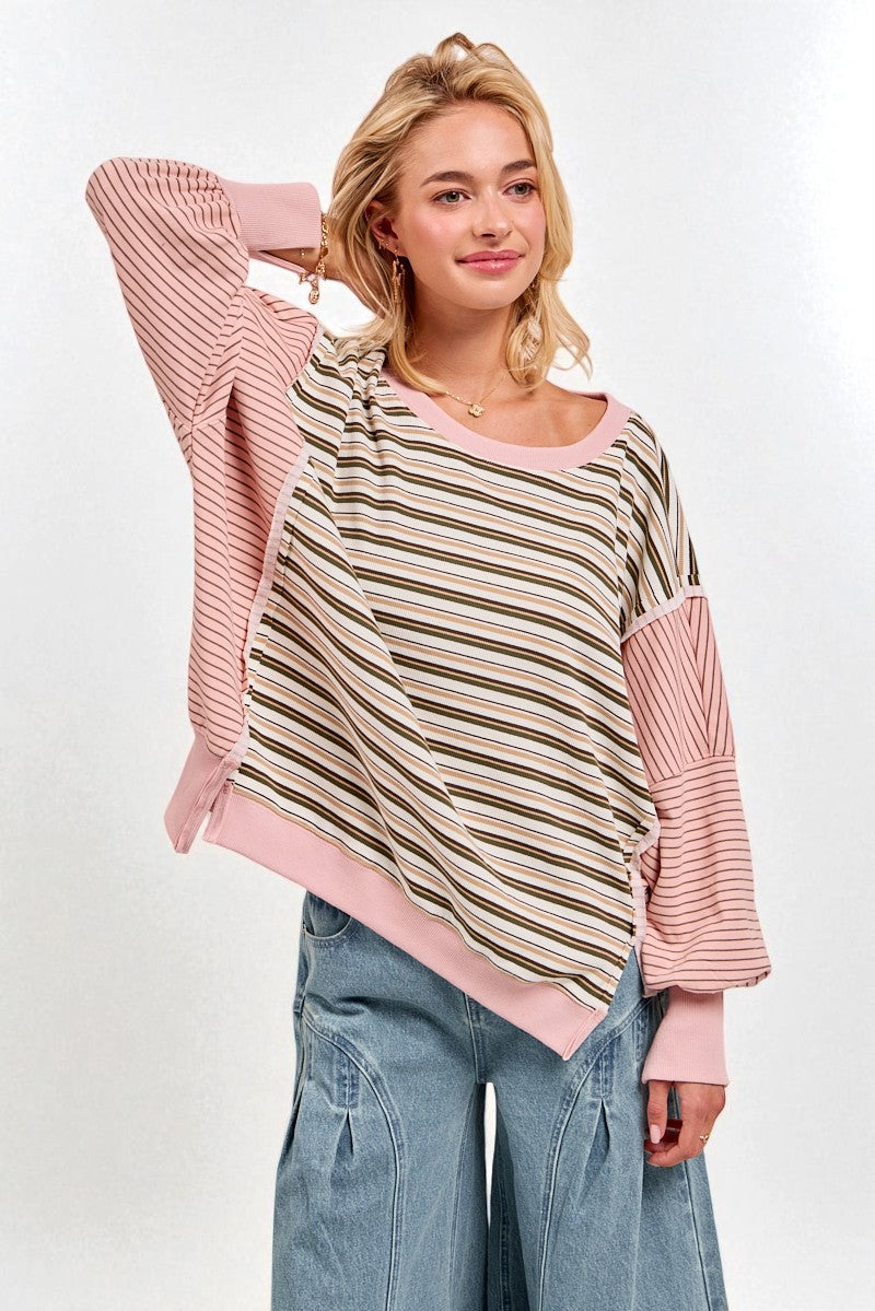 Woman wearing a striped sweater with pink sleeves and a beige center, standing against a white background.