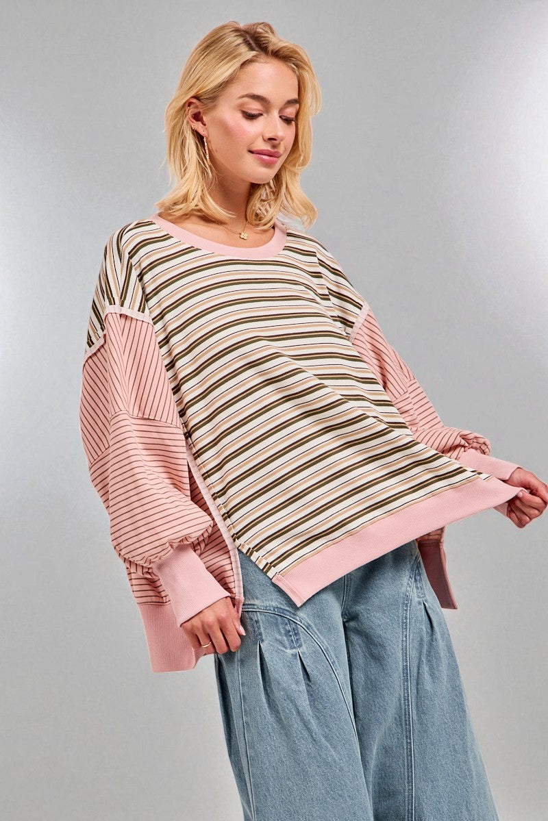 Woman wearing a striped sweater with pink sleeves and a neutral patterned center against a gray background