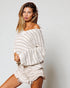Woman wearing a white off-shoulder sweater and shorts against a plain background