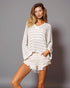 Woman wearing a white striped sweater and denim shorts against a gray background