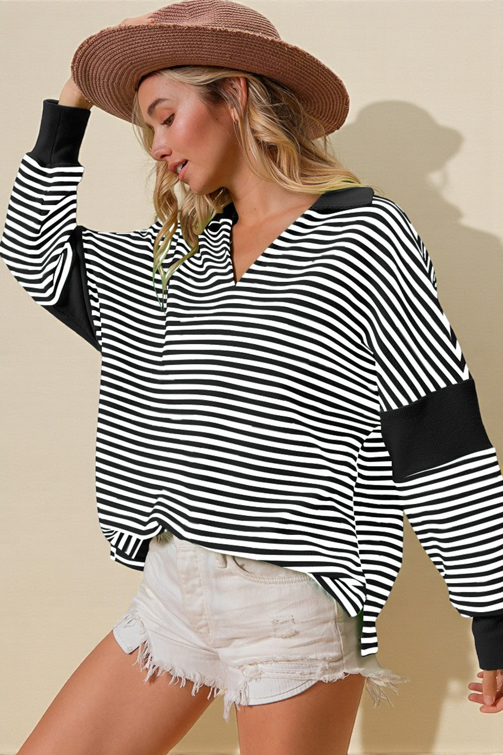 Woman wearing a black and white striped shirt with elbow patches and a brown hat on a beige background