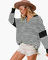 A woman wearing a black and white horizontally striped long-sleeve top with solid black contrast panels on the shoulders and cuffs, paired with distressed white denim shorts and a brown straw hat, against a plain white background.