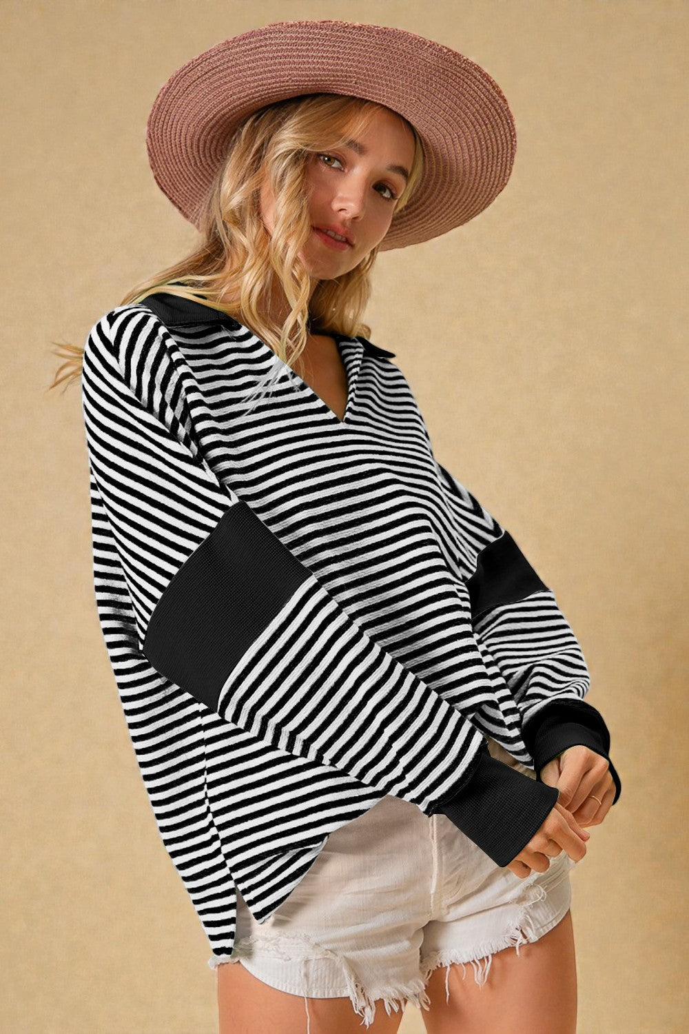 Woman wearing a black and white striped long-sleeve top with a pink hat on a beige background