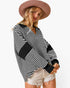 A woman wearing a black and white striped long-sleeve top with solid black patchwork panels on the shoulders and sleeves, paired with light denim shorts and a wide-brimmed brown hat, against a plain white background.