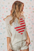 Person wearing a white sweater with a red heart design on a patterned background