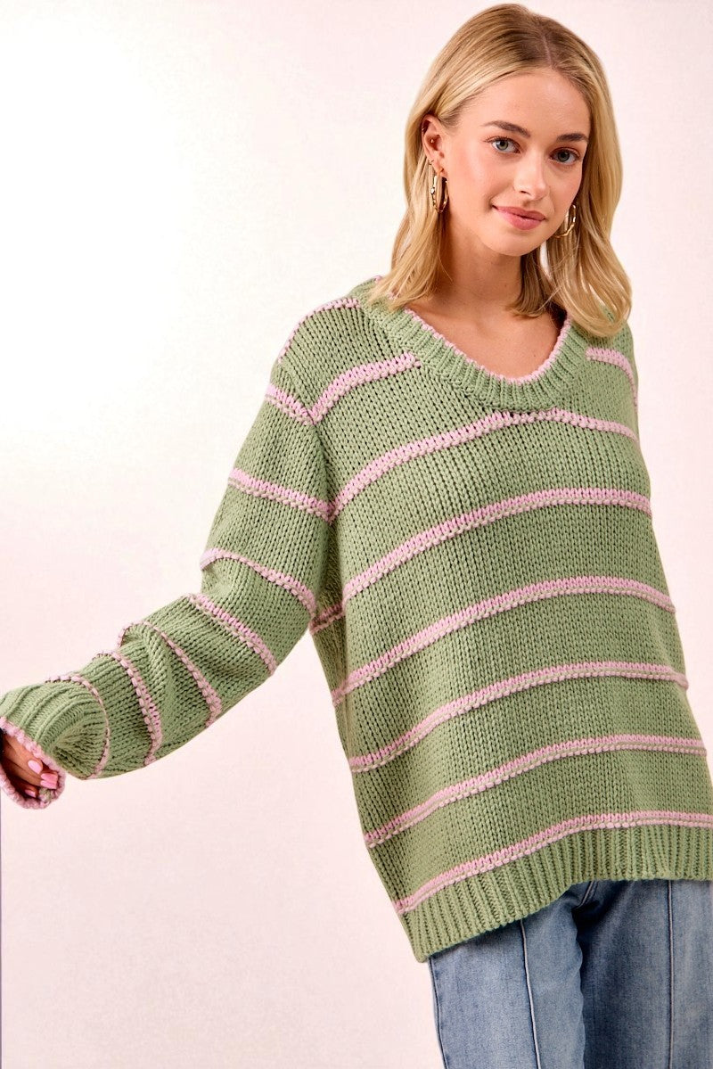 Woman wearing a green sweater with pink stripes on a light pink background