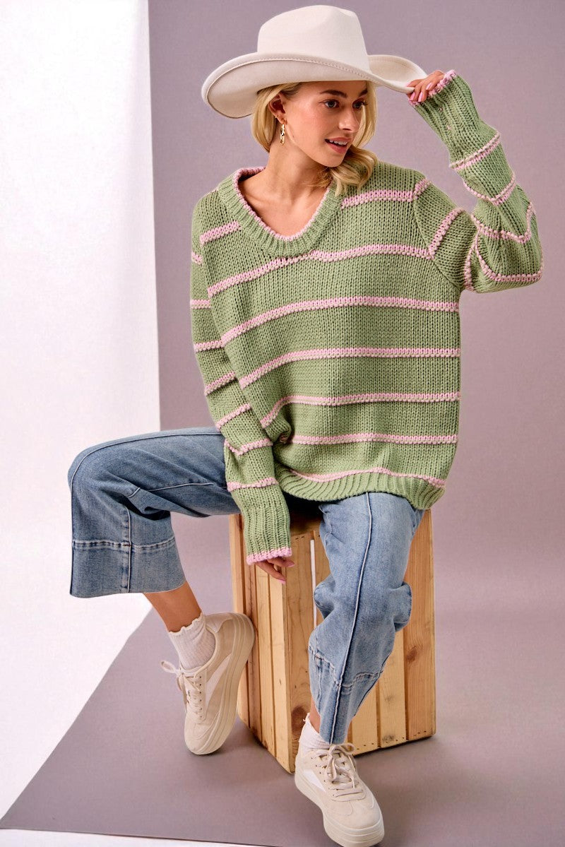 Woman wearing a green striped sweater and white hat, sitting on a wooden stool.