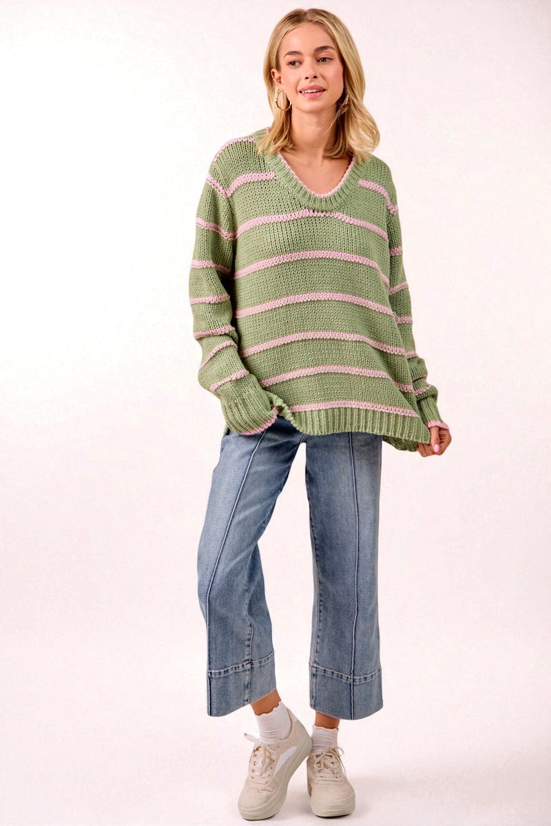 Woman wearing a green and pink striped sweater with blue jeans on a white background
