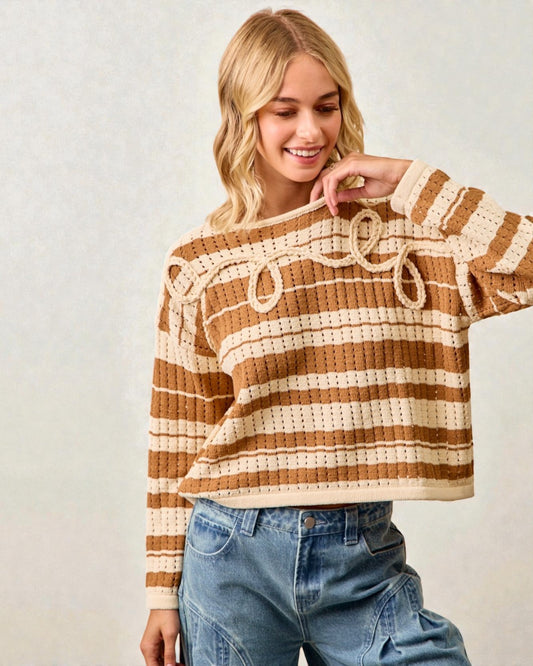 Woman wearing a brown and beige striped sweater with blue jeans on a plain background
