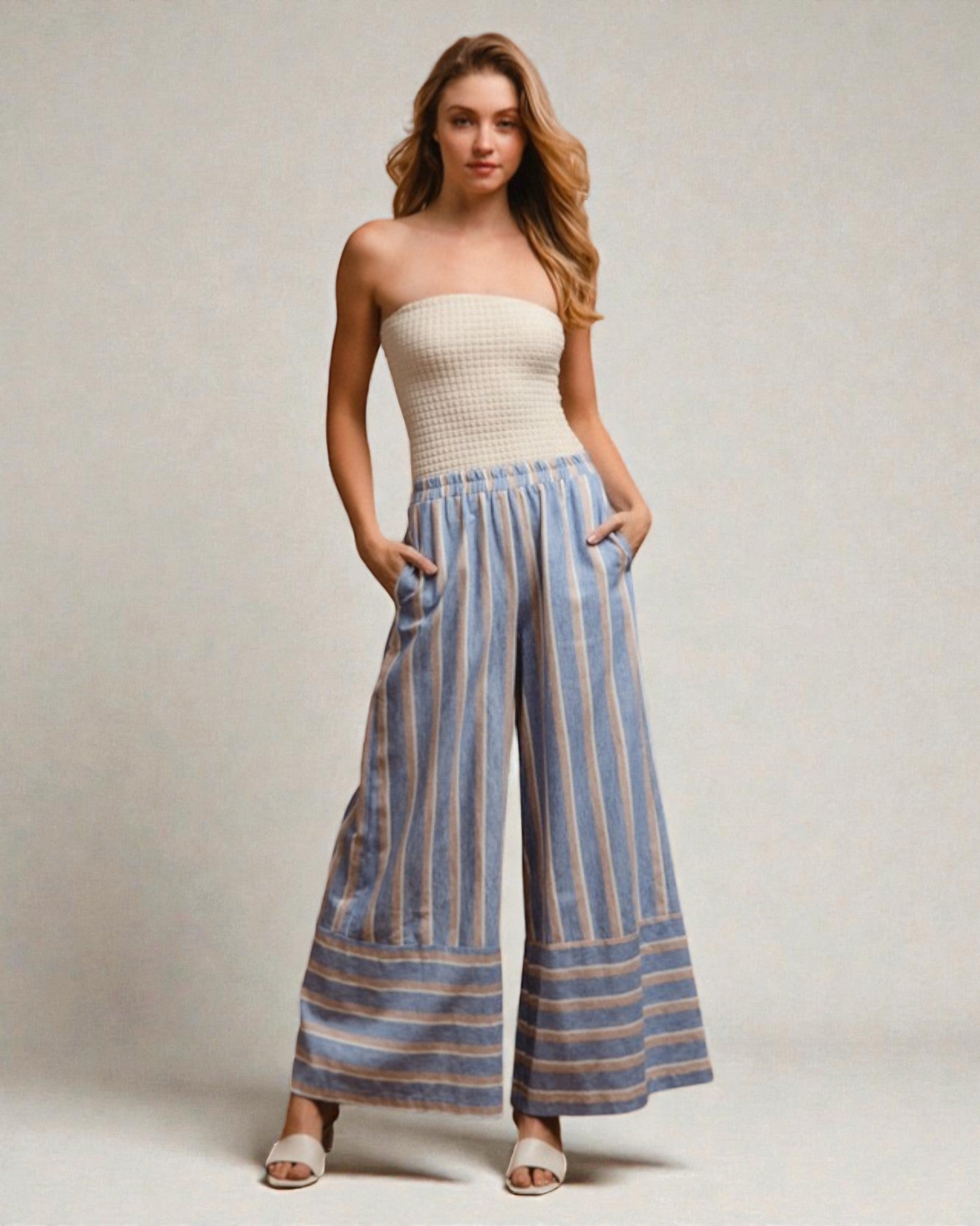 Woman wearing a strapless top and blue striped pants on a plain background