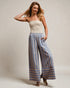 Woman wearing a strapless top and striped pants against a plain background